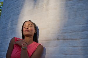 woman basking in sunlight in front of a white brick wall