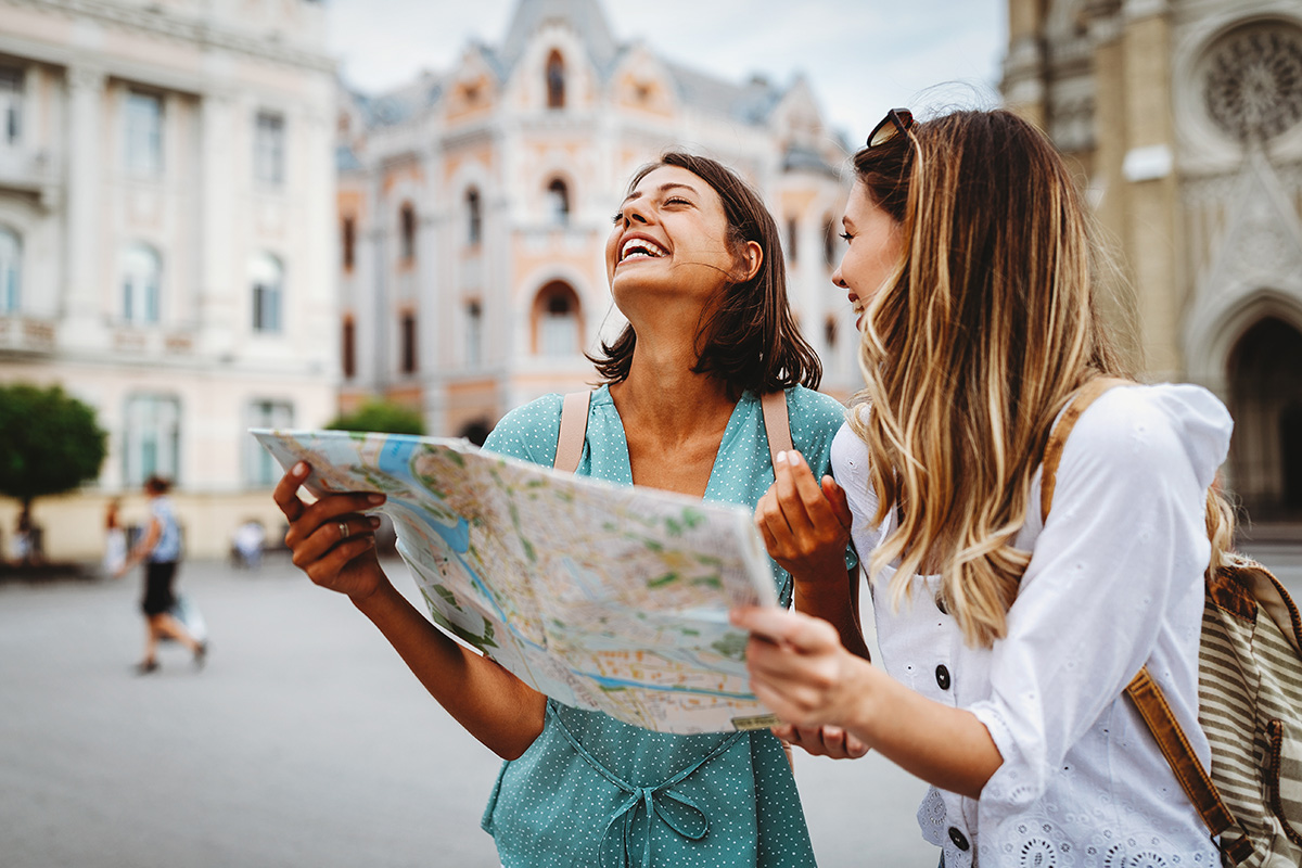 Two happy women exploring a city, laughing while looking at a map.