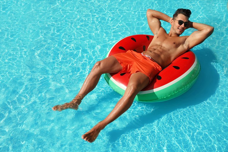 Man in red swim trunks lounging in a watermelon-shaped floatie in the pool.
