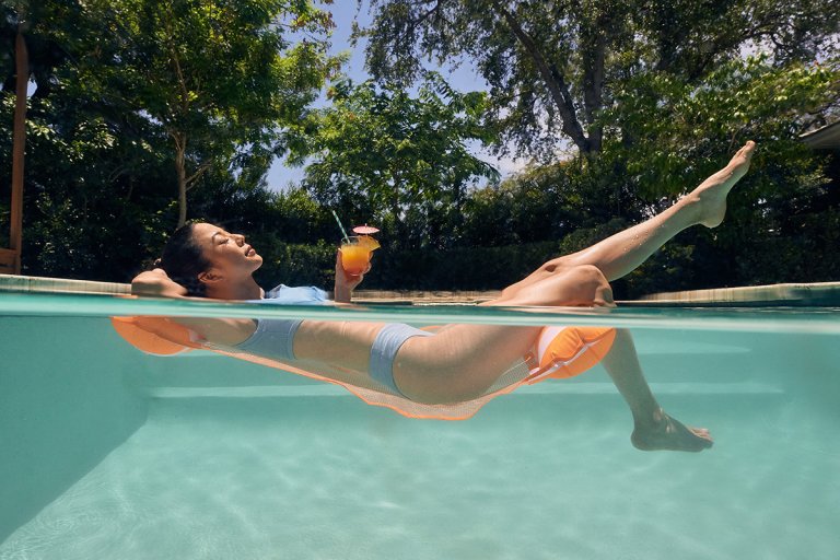 Woman with waxed legs floating in a pool with a fruit drink