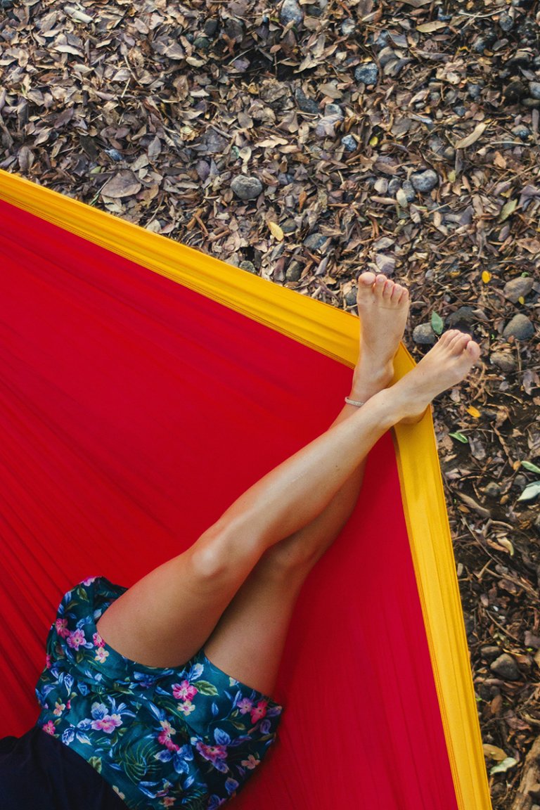 A person lying in a red hammock, with smooth, waxed legs.