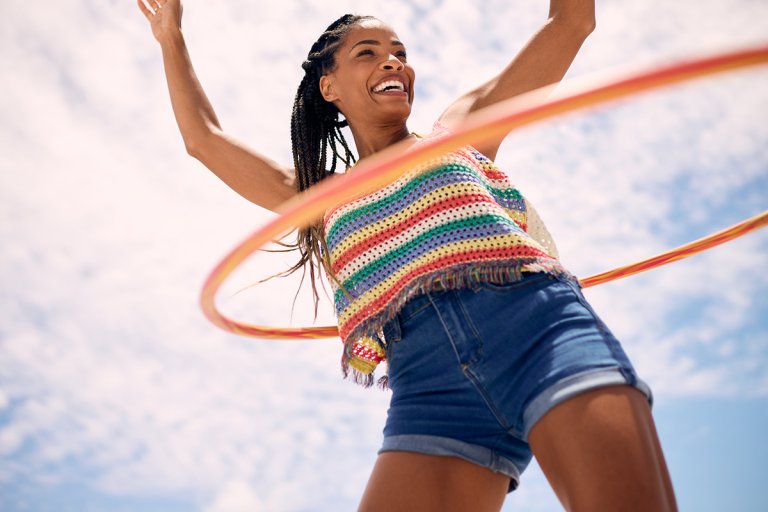 A woman hula-hooping with a blue sky behind her.