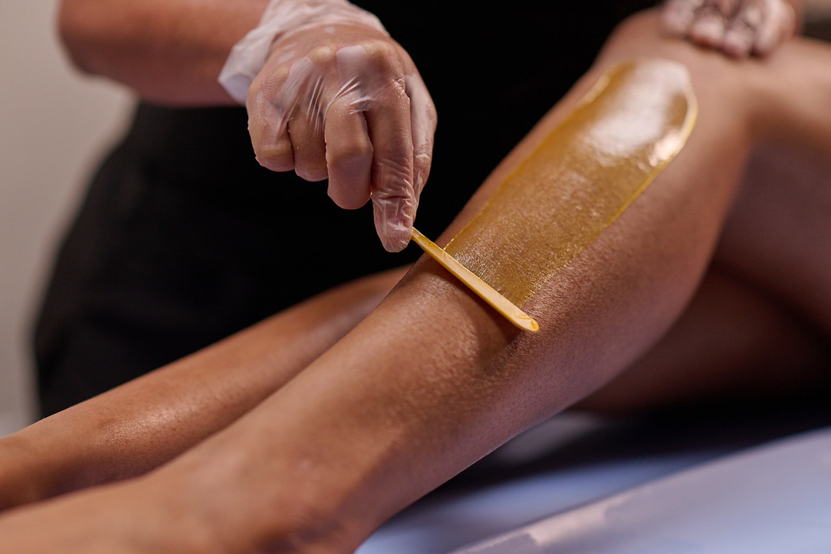 Close-up of bare legs on a spa table with a professional applying wax to one of the legs.