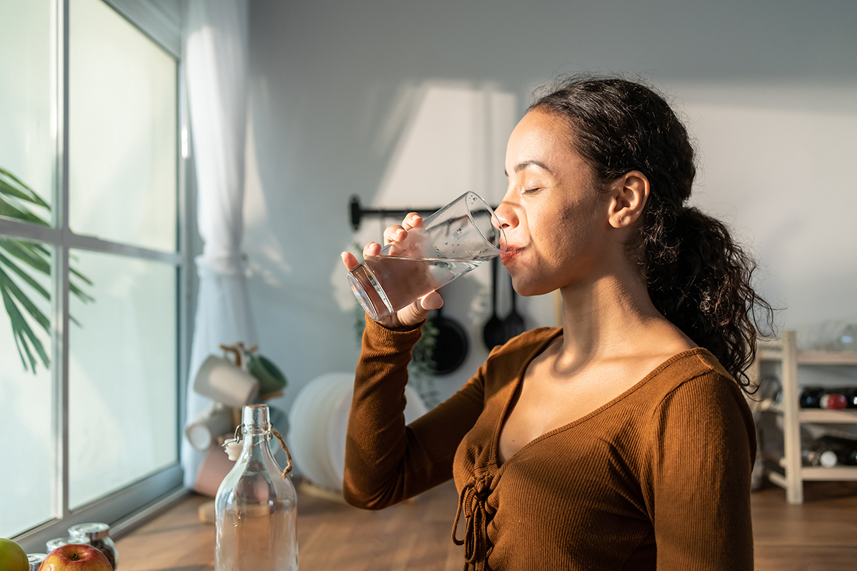 Woman in a bright room drinking a glass of water.