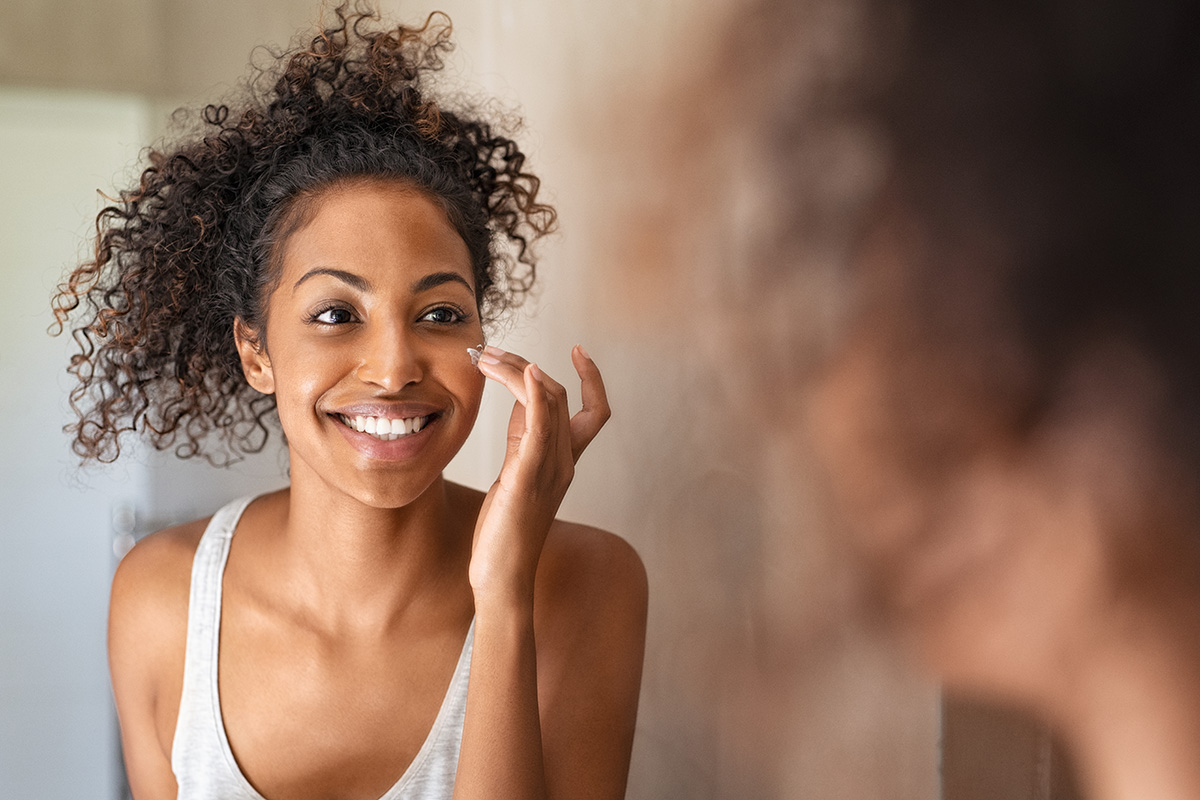 Woman with curly hair applying moisturizer to her face, showcasing a skincare routine for radiant skin.