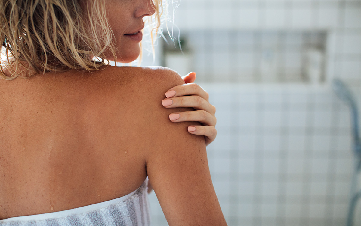 Close-up of a woman’s shoulder, gently moisturizing skin post-shower to maintain hydration.