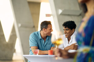 Two men enjoying drinks and a casual conversation outdoors, promoting relaxation and self-care as part of a pre-waxing routine.