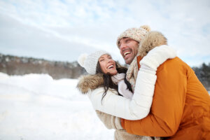 A happy couple dressed in winter coats and hats, enjoying snowy outdoors while maintaining glowing, hydrated skin in cold weather.