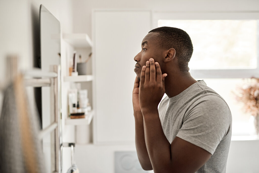 A man examining his face in the mirror indoors, emphasizing the importance of a winter skincare routine to combat dryness during cold months.